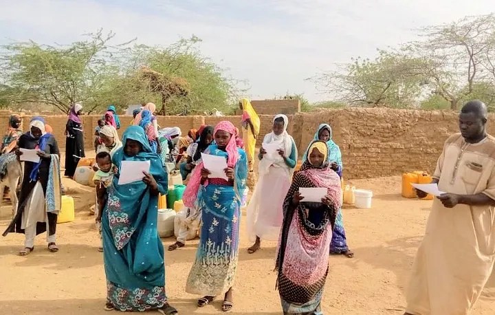Community in a refugee camp reading COVID-19 fact sheets.